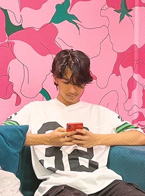 Sitting on a couch looking at a phone against a pink floral backdrop